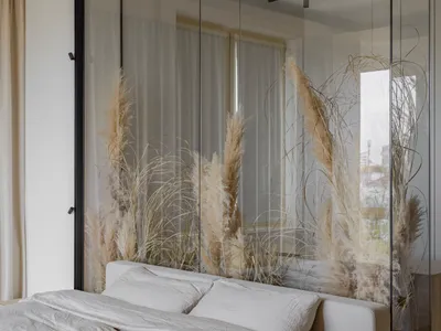 Bedroom featuring a bed with white bedding and pampas grass, behind a glass partition.