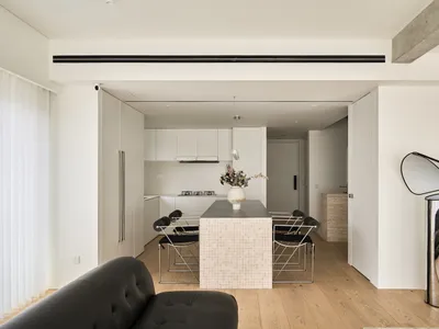 A minimalist kitchen and dining area featuring a marble-topped tile island and sleek black chairs.