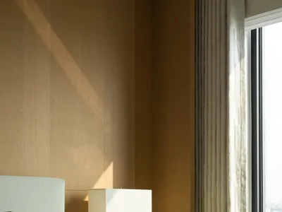 A modern minimalist bedroom featuring a wooden bed frame, fabric bedding, and a glass lamp and vase with white tulips.