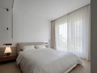 A minimalist bedroom with a neatly made bed, white sheets, and a hanging light bulb.