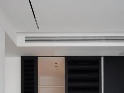 A minimalist bedroom with a white bed, black sliding shutters, and wooden flooring.