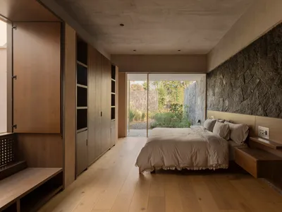 Minimalist bedroom featuring hardwood flooring and a stone wall.
