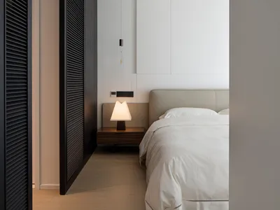 Minimalist bedroom with a wooden floor, white bedding, and a lamp on the bedside table.