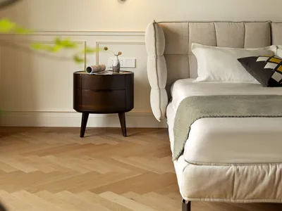 A modern minimalist bedroom featuring a beige upholstered bed with a wooden bedside table and a sleek, wall-mounted lamp.