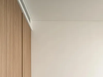Minimalist bedroom with light wood flooring, a beige upholstered bed, and a patterned side table with a mug and book.