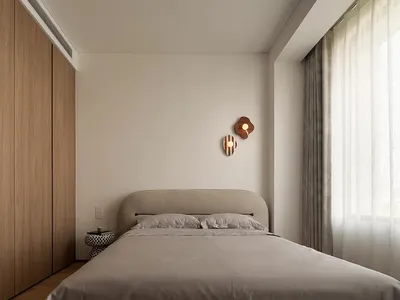 A minimalist bedroom featuring a bed with a neutral-colored headboard and bedspread, along with a simple nightstand and decor