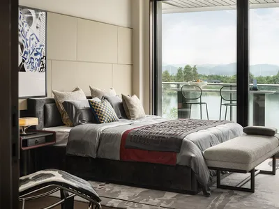 A modern bedroom with fabric bedding, a wooden floor, and a glass door overlooking a scenic landscape.