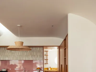 A modern kitchen with wooden floors, pink tiles, and white bar stools.