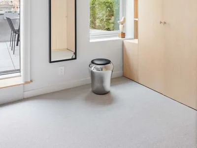 A minimalist bedroom featuring sleek concrete and wooden furniture, with a soft, textured rug.