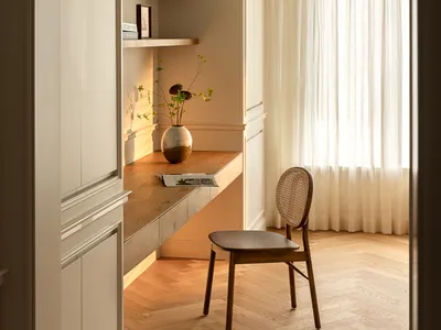 A minimalist home office with a desk, chair, bookshelf, and curtain.