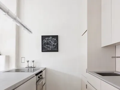 A minimalist white kitchen with a wooden floor, stainless steel appliances, and concrete countertops.