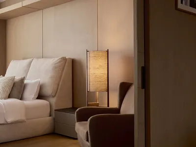 A modern minimalist bedroom featuring a wooden floor, upholstered furniture, and a floor lamp with a woven shade.