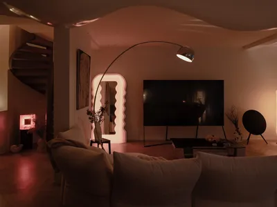 Modern living room with minimalist decor, featuring a curved floor lamp, a television, and comfortable seating.