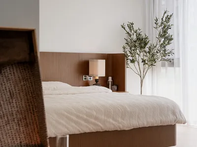 A minimalist bedroom featuring a wooden bed and a large window with sheer curtains.