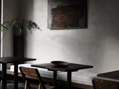 A minimalist restaurant interior featuring concrete walls and wooden furniture.