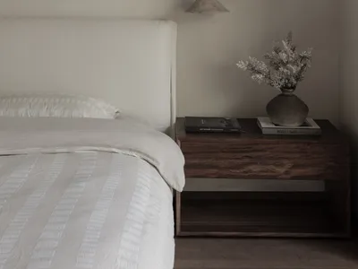 Minimalist bedroom with white bedding and a wooden nightstand.