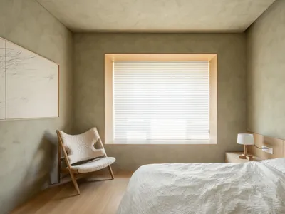 Minimalist bedroom with wooden furniture, concrete walls, and soft textiles