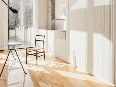 A modern home office featuring wooden flooring and a glass table with a black lamp and a wooden chair.
