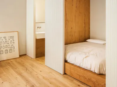 A minimalist bedroom featuring wooden walls and a bed with a wooden frame and white bedding.