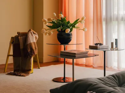 A cozy living room with a gray sofa, orange curtains, and white tulips in a vase on a glass table.