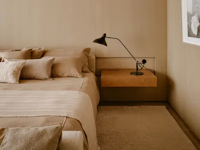 Modern minimalist bedroom with wooden walls and headboard, featuring a bed, nightstand with a lamp, and artwork on the wall.