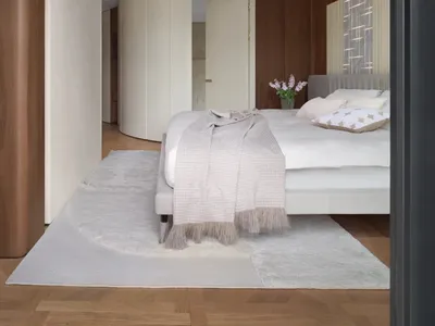 Modern, minimalist bedroom featuring wooden paneled walls, white closets, porcelain floor tiles, and a gray rug. The space is