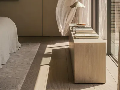 Minimalist bedroom interior with a bed, a window with sheer curtains, and a nightstand with a lamp and books.