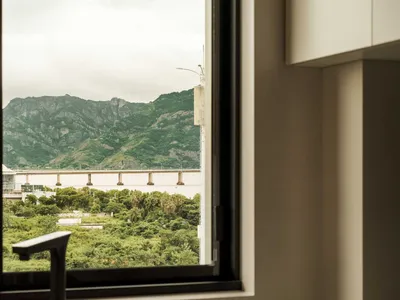 一間以混凝土飾面呈現的現代簡約廚房，透過窗戶可眺望山景與橋樑。