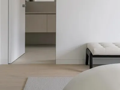 Modern minimalist white bedroom suite with neutral tones, clear glass shower enclosure, white bedding, and sleek black accent