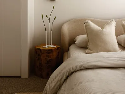 Minimalist bedroom with light-colored bedding and neutral-toned walls and flooring.