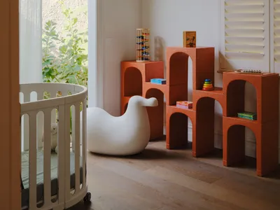 A modern children's bedroom featuring white furniture with bird-shaped armé and orange modular shelving units with children's