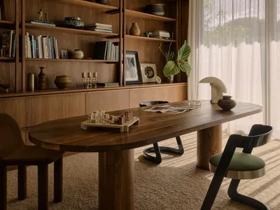 A modern home office with wooden furniture, a large oval table, and a bookshelf.