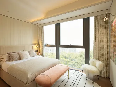 A modern bedroom with a large window, a comfortable bed with plush bedding, and a cozy seating area with a fur-covered chair