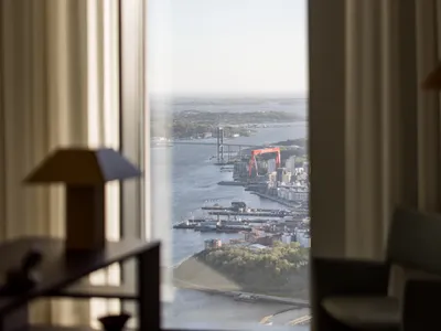 A modern hotel room with a view through transparent glass curtains, featuring leather furniture and a serene waterfront setti