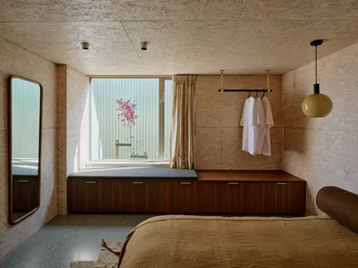 Minimalist bedroom with concrete floor, wooden bench, and hanging garments