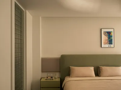 Minimalistic bedroom featuring a green upholstered bed with neutral textiles and a sleek nightstand.