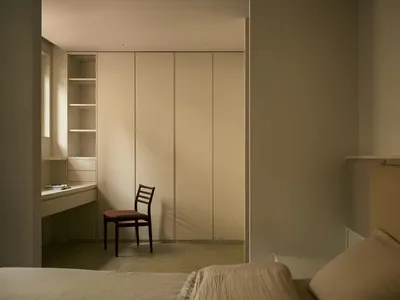 A minimalist bedroom featuring a bed with a neutral-toned upholstered headboard and a beige space-saving wardrobe with a buil