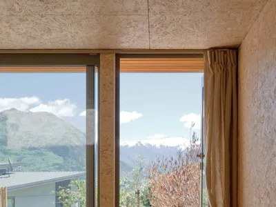 A minimalist bedroom with wood paneling, a glass window, and a metal stool.