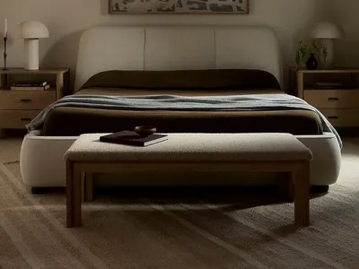 A modern minimalist bedroom with plush fabric bedding and wooden furniture.