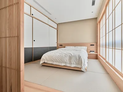 A modern minimalist bedroom with a wooden bed and white fabric bedding on tatami mats.