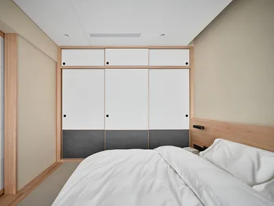 Minimalist bedroom with white walls, wooden floor, and a bed with white bedding.