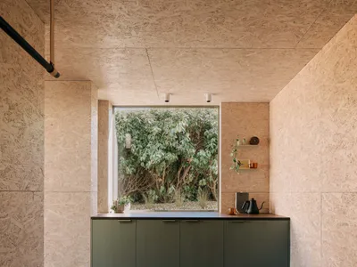 A modern minimalist kitchen with concrete walls and cabinets, featuring a small window with a view of greenery.