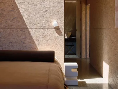 A minimalist bedroom featuring OSB board walls and a sleek, modern bed