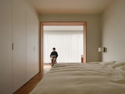 A minimalist bedroom with white textured fabric and wooden floor.