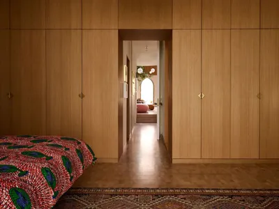 A minimalist bedroom with a bed featuring a red and green patterned blanket placed on a wooden rug.