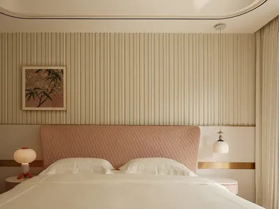 A minimalist bedroom featuring a pink upholstered headboard with geometric patterns, white bedding, and a geometric-patterned