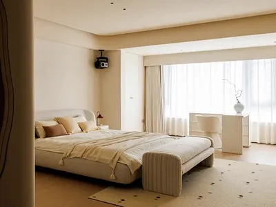 A minimalist bedroom featuring a bed with fabric bedding, a soft, cushioned bench at the foot, and a large window with sheer