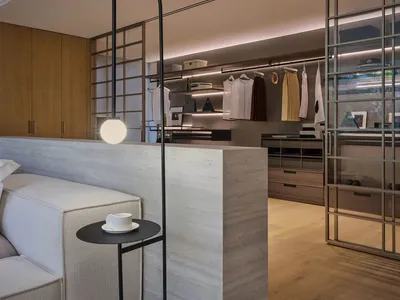A modern bedroom featuring a bed with a white headboard, a side table with a black lamp and a cup of coffee, and a closet wit
