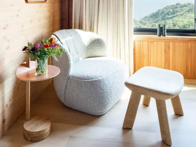 A cozy, minimalist living room with a cozy, white, plush armchair adorned with white cushions nestled in a cozy nook, illumin