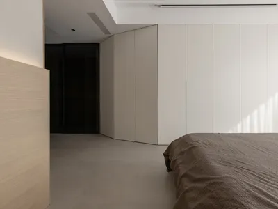 Modern minimalist bedroom with concrete floor and walls and a large bed with a gray textured blanket.